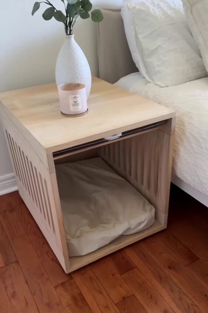 Natural birch wood dog crate end table with sliding door next to a bed