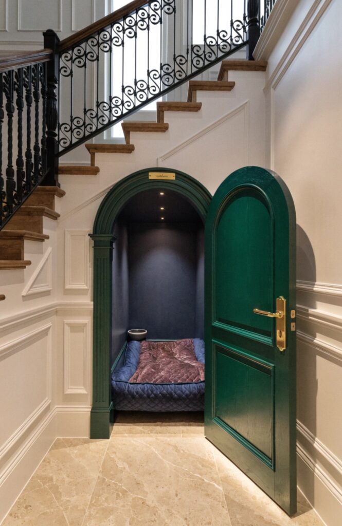 luxury dog kennel suite beneath a staircase with arched green door and gold hardware