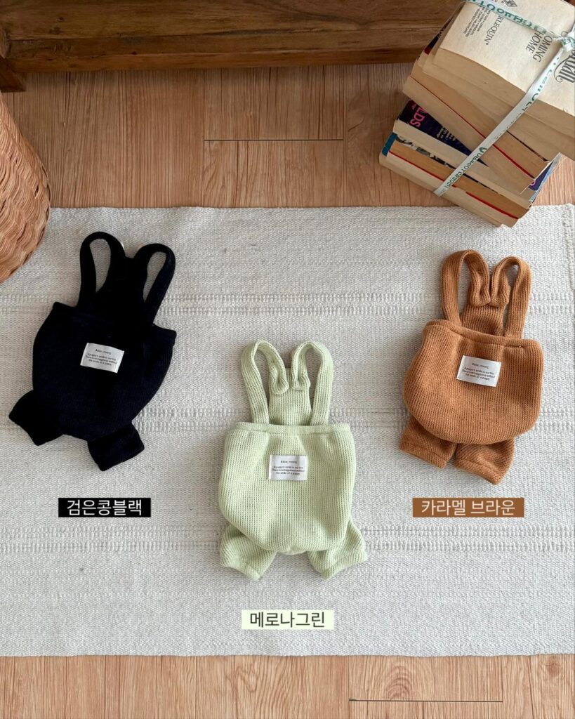 three knitted dog rompers with bunny ear straps in black sage green and caramel flat lay