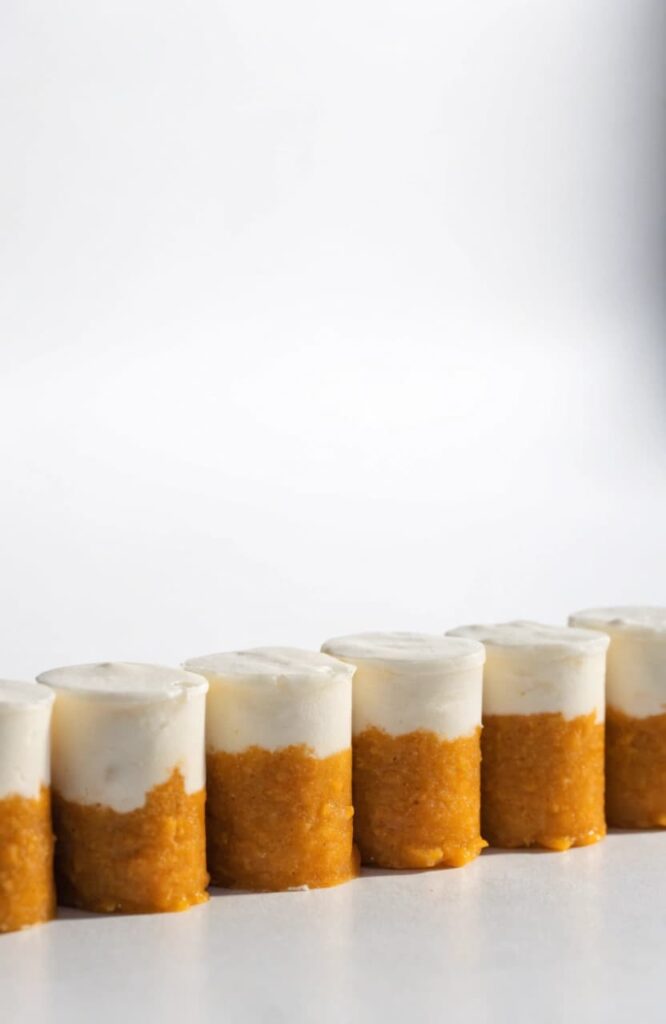 Layered pumpkin and yogurt dog treat cups lined up in a studio shot