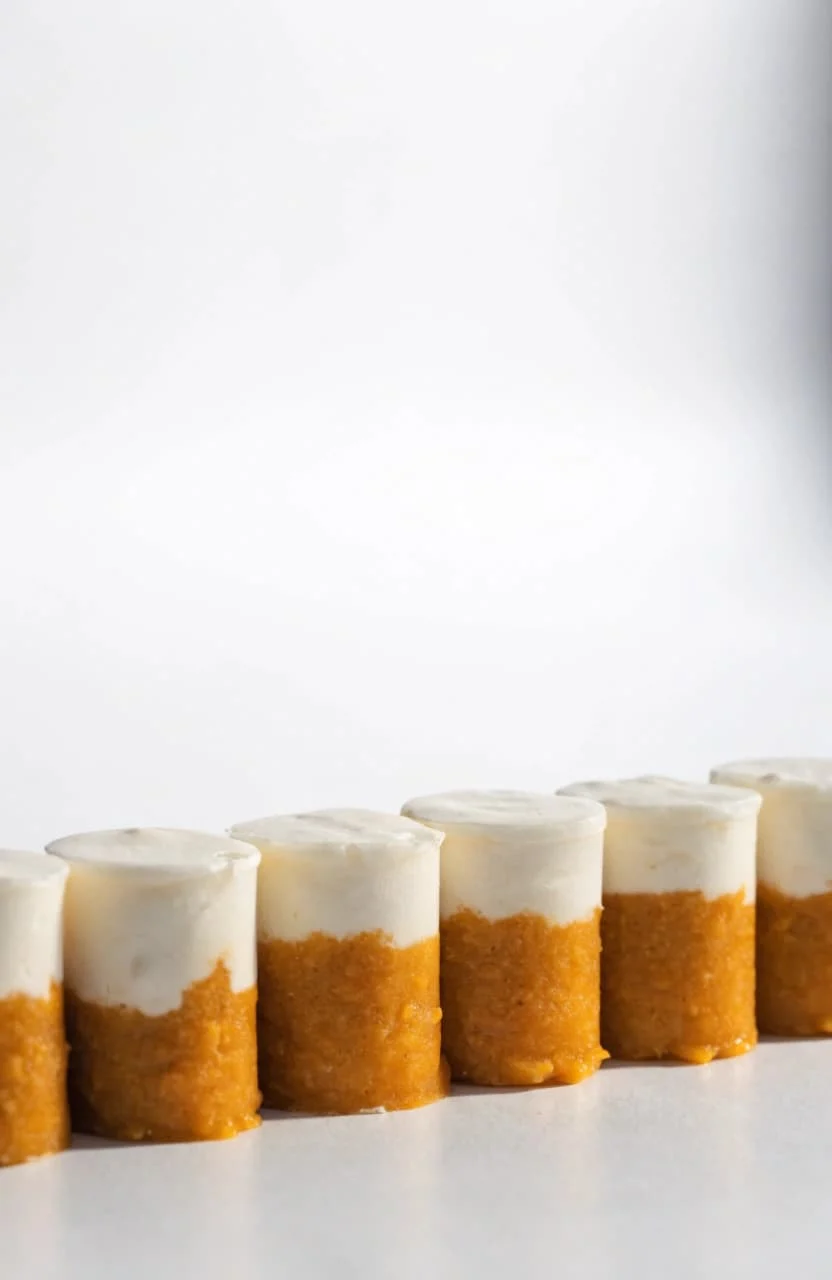 Layered pumpkin and yogurt dog treat cups lined up in a studio shot