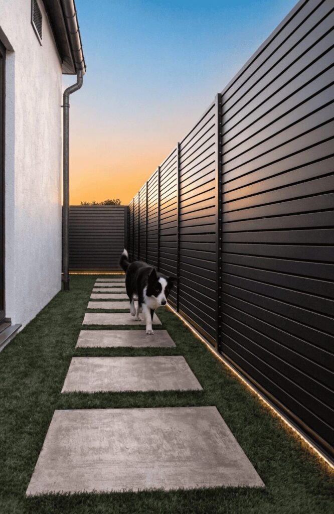 Minimalist modern side-yard dog run with black steel fence and concrete stepping stones