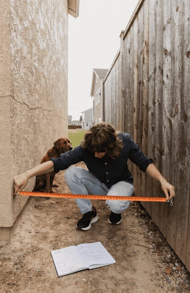 Homeowner planning a side-yard dog run with tape measure and yard sketch