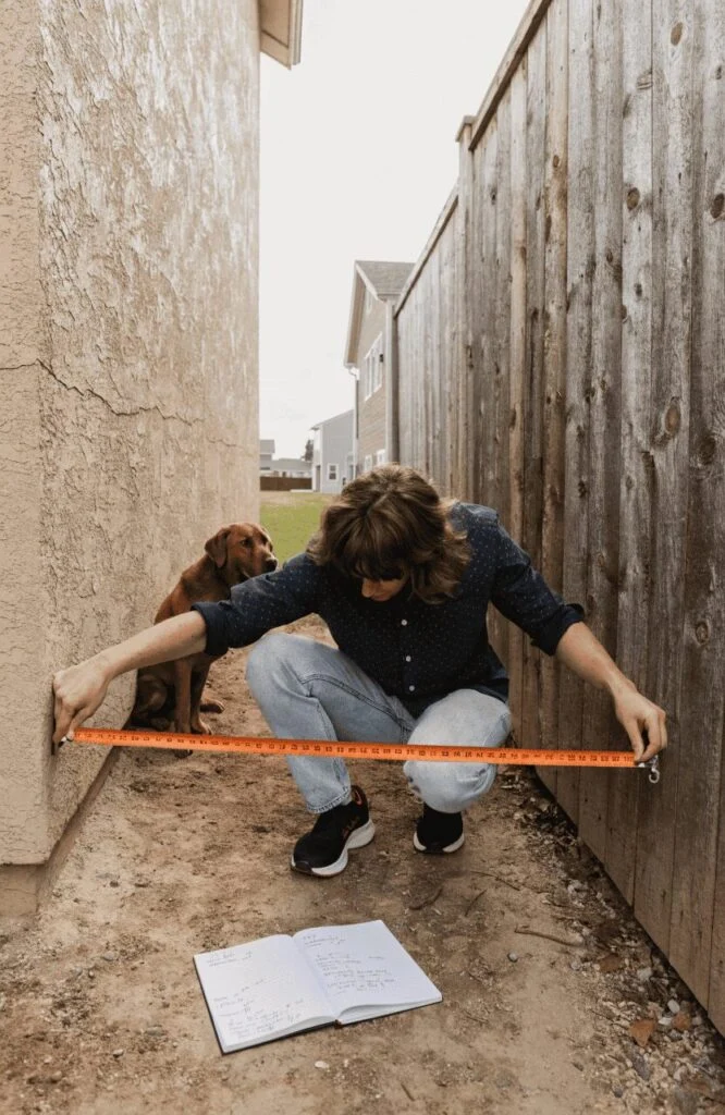 Homeowner planning a side-yard dog run with tape measure and yard sketch