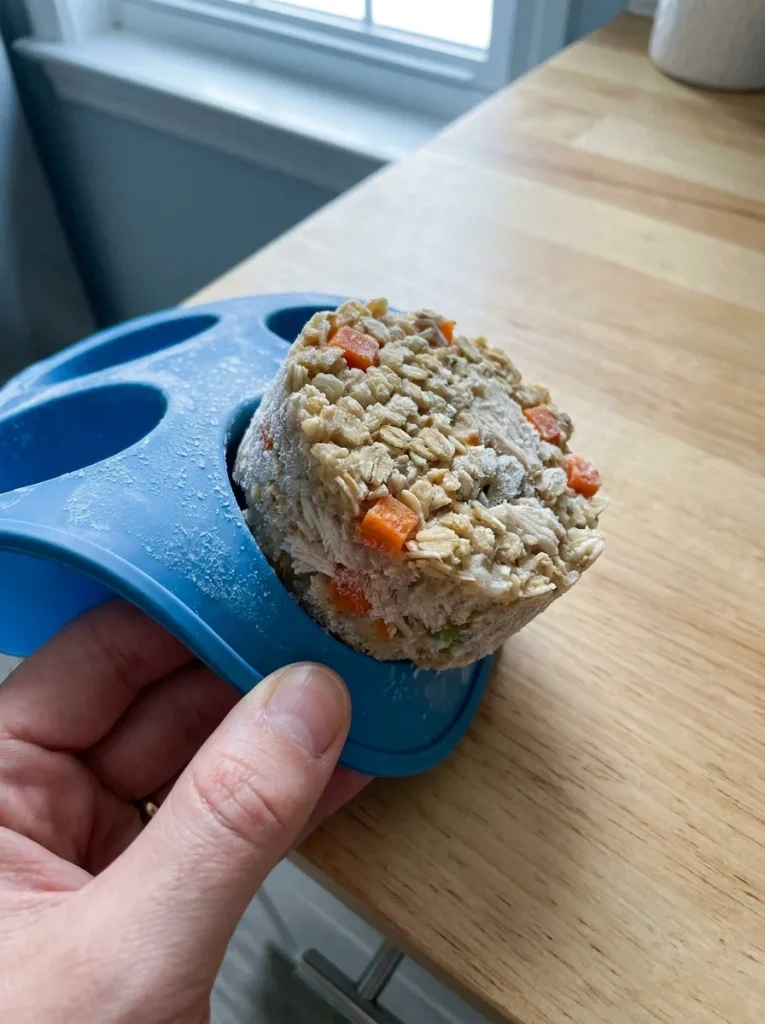 Hand removing a frozen cup from the Chicken & Oatmeal Dog Food Recipe tray